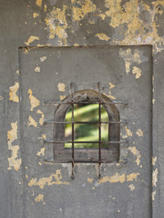 Weathered painted wall with a small window with an iron lattice.