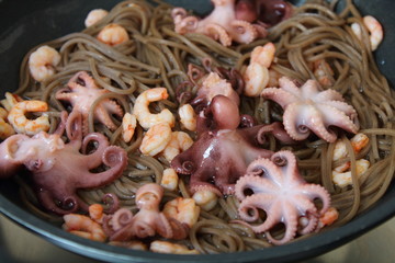 Seafood and noodles in a pan. Shrimps, octopus and buckwheat noodles in a skillet.