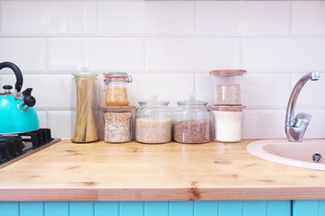 Glass jars with products. Blue kitchen with wooden top. Kettle on the stove..