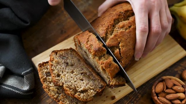 Slicing banana bread. Hands slicing homemade banana bread with nuts on a cutting board