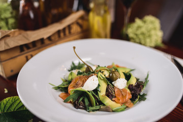 salad with salmon, avocado and cheese on a white plate.