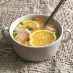 Delicious chicken soup with lemon, rise, carrot and green onion. Soup cup with a spoon on a table. Rustic tablecloth.