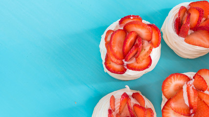 A small meringue Pavlova dessert with some strawberry slices on a blue background. Top view.