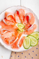 plate with slices of salmon fillet decorated with cucumber and greens