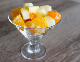 Fresh fruits salad in the glass cup, apples and oranges fresh, wooden background