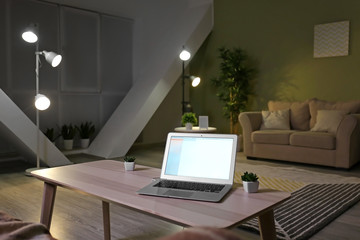 Modern laptop on table in living room at night