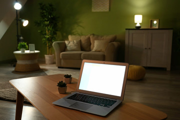Modern laptop on table in living room at night