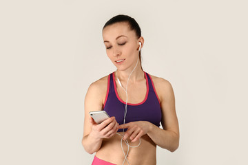 Sporty woman listening to music on light background