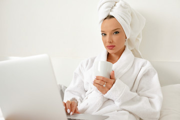 Waking up in a hotel, a young girl, a blogger, gladly does her job with a cup of freshly brewed coffee.