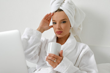 Waking up in a hotel, a young girl, a blogger, gladly does her job with a cup of freshly brewed coffee.