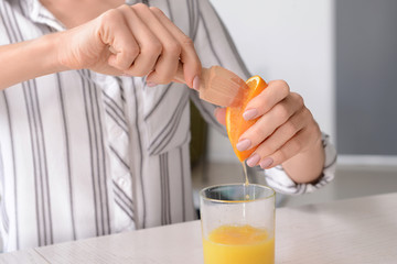 Beautiful young woman squeezing juice from orange at home, closeup