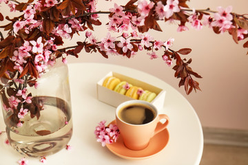 Vase with beautiful blossoming branches and cup of coffee on table