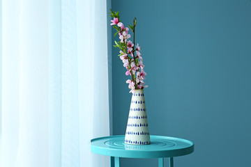Vase with beautiful blossoming branches on table near window in room