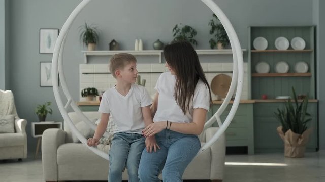 Young mother and son having fun on swing in living room. Happy family spending time together, playing and hugging.