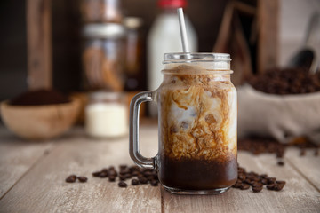 Glass jar of iced mocha latte coffee with a straw on wooden table with ingredients, copy space