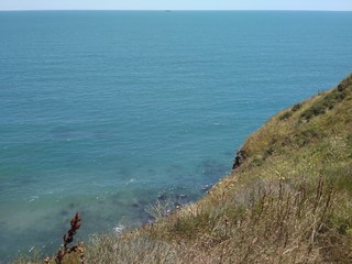 The view from the cliff to the turquoise sea, a strip of blue sky and a ship on the horizon at Cape Kaliakra.