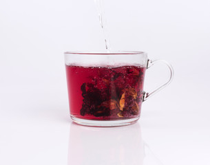 Pouring hot water to the glass cup with hibiscus tea, isolated on white background