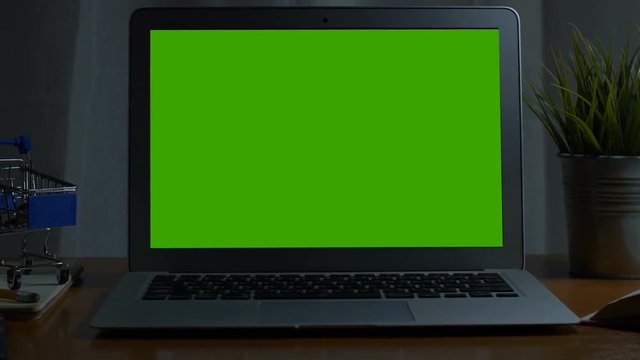 Laptop with green screen. Dark office. Dolly in. Perfect to put your own image or video. Track with perspective corner pin.  Green screen of technology being use.