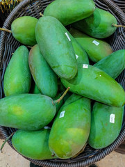 Bulk green mangoes with labels in a basket
