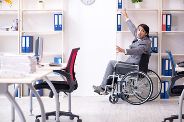 Young handsome employee in wheelchair working in the office  
