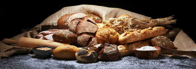 Assortment of baked bread and bread rolls on rustic grey bakery table background