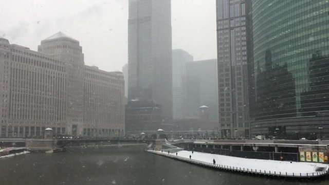 Snow falling across Chicago River as commuters brave the weather on the riverwalk.