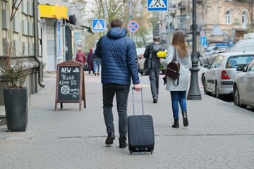 Man in jacket with suitcase walking down city street, back view