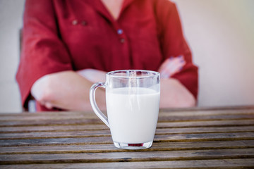 Sad woman on background and glass of milk on a table on foreground