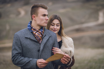 A nice beautiful lovely couple in the park or field. man in Gray coat and scarf with girl woman in brown coat. lady put her head on his shoulder hugged behind. lovers keep and read paper letter