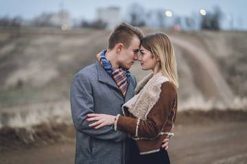 lovers close up emotional portrait. man hugs women. beautiful lovely fashionable trendy stylish couple hugging kissing. man in coat and scarf with woman in coat. lovers leaned touched foreheads