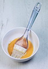 BOWL WITH SHAVE EGG AND KITCHEN BRUSH ON WOODEN BACKGROUND