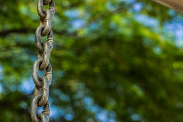 dangerous for ecology concept photography pattern of old iron chain hanging on unfocused blurred natural green park outdoor background, empty copy space for text or inscription 
