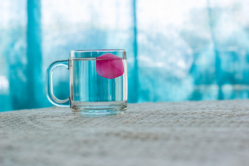 cup of water with red peace of ice on a table in indoor cafe interior blurred background with blue curtains, summer hot season time concept wallpaper pattern with empty copy space for text 