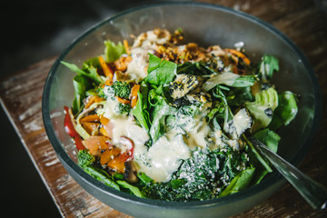 Vegan salad with various veggies and greens, and dressing in a glass bowl on a wooden table. Closeup, food blog, healthy eating, recipe