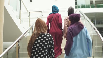 Multiracial group of muslim business women visiting international conference at business centre, walking up the staircase sharing impressions and ideas after event