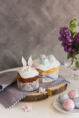 Easter Cakes on wooden decorated with rabbit ears, eggs on whith plate on foreground, lilac on background. - Traditional Kulich, Paska Easter Bread