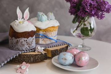 Easter Cakes on wooden decorated with rabbit ears, eggs on whith plate on foreground, lilac on background. - Traditional Kulich, Paska Easter Bread