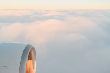 The view from the airplane's illuminator to the wing, airplane turbine and fluffy clouds at sunrise. Flying over the clouds