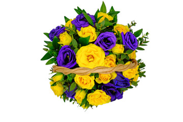 Basket with yellow and blue flowers on isolated white background. Top view of a bouquet of yellow and violet roses. Beautiful flowers in a wicker basket with a wooden handle.