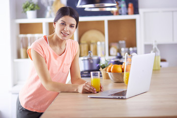 Young woman in kitchen with laptop computer looking recipes, smiling. Food blogger concept