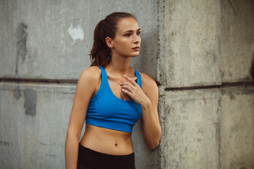 young attractive woman in sportswear near concrete wall, looking right, outdoor workout