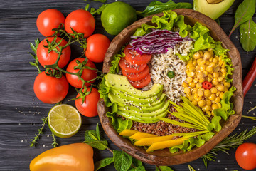 Buddha bowl with chickpea, avocado, wild rice, quinoa seeds, bell pepper, tomatoes, greens, cabbage, lettuce on old black wooden table. Top view. Healthy vegan food.