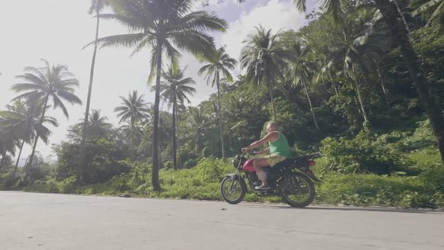 Senior man riding motorbike on road on sunshine background. Mature man riding motorcycle on green palm trees landscape. Motorcycle lifestyle.