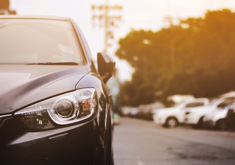Focusing on the black car headlights on a street corner with sunlight flares, In the background, the driver and car. Car parking on the street. space for insert text.
