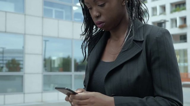 confident african american business woman walking typing on her smartphone