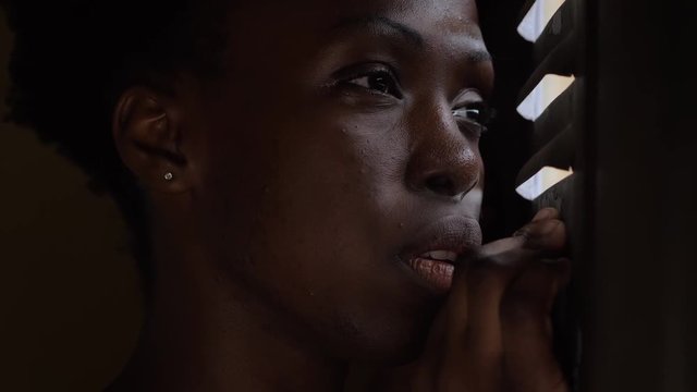 young abused black woman hiding behind the window in the dark. Fear, violence