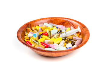 Bowl of multicolored pills and syringes addiction concept