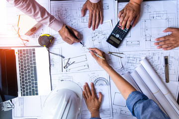 engineers pointing to building on blueprint and using laptop to drawing design building Project in office, construction concept. Engineer concept