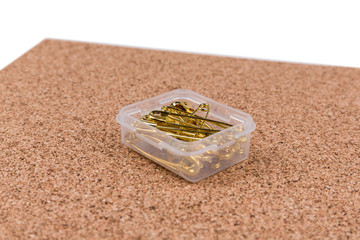 Gold safety pins in a container on a piece of cork board