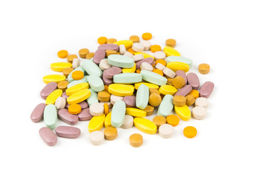 Pile of green orange purple and yellow pills over a white background